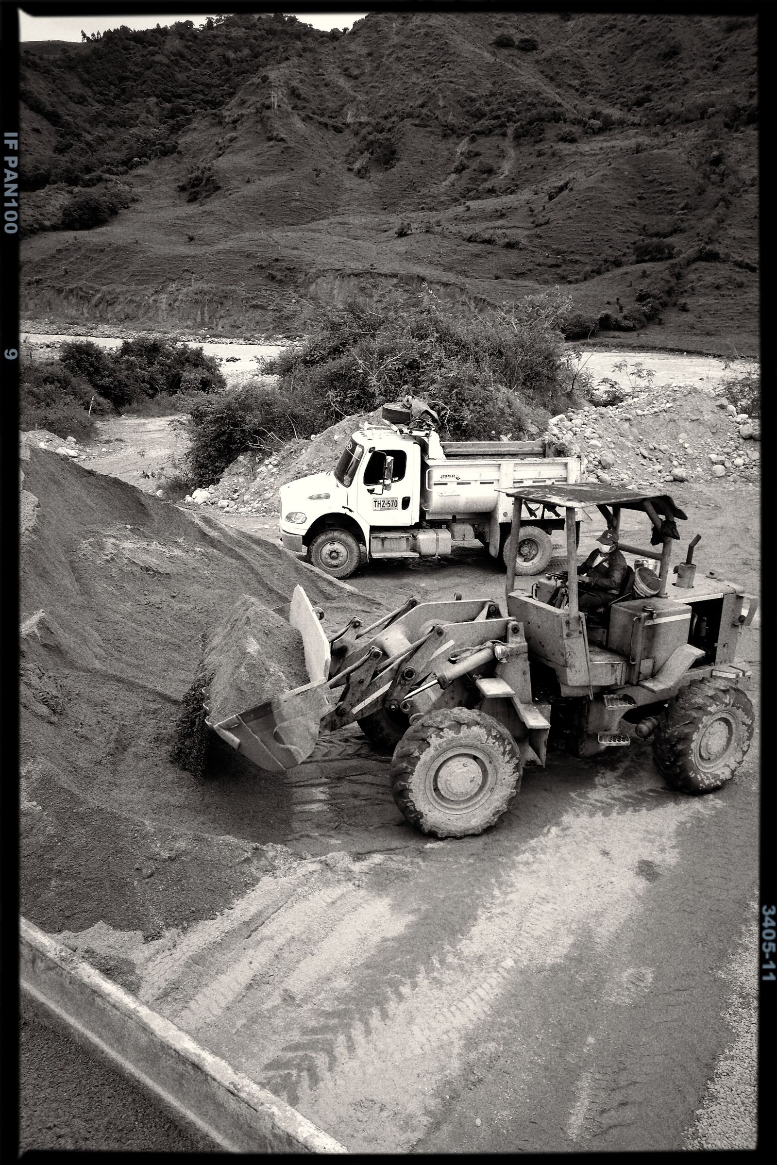 Front end loader loading a gravel pile with a tipper truck behind, hills in the background